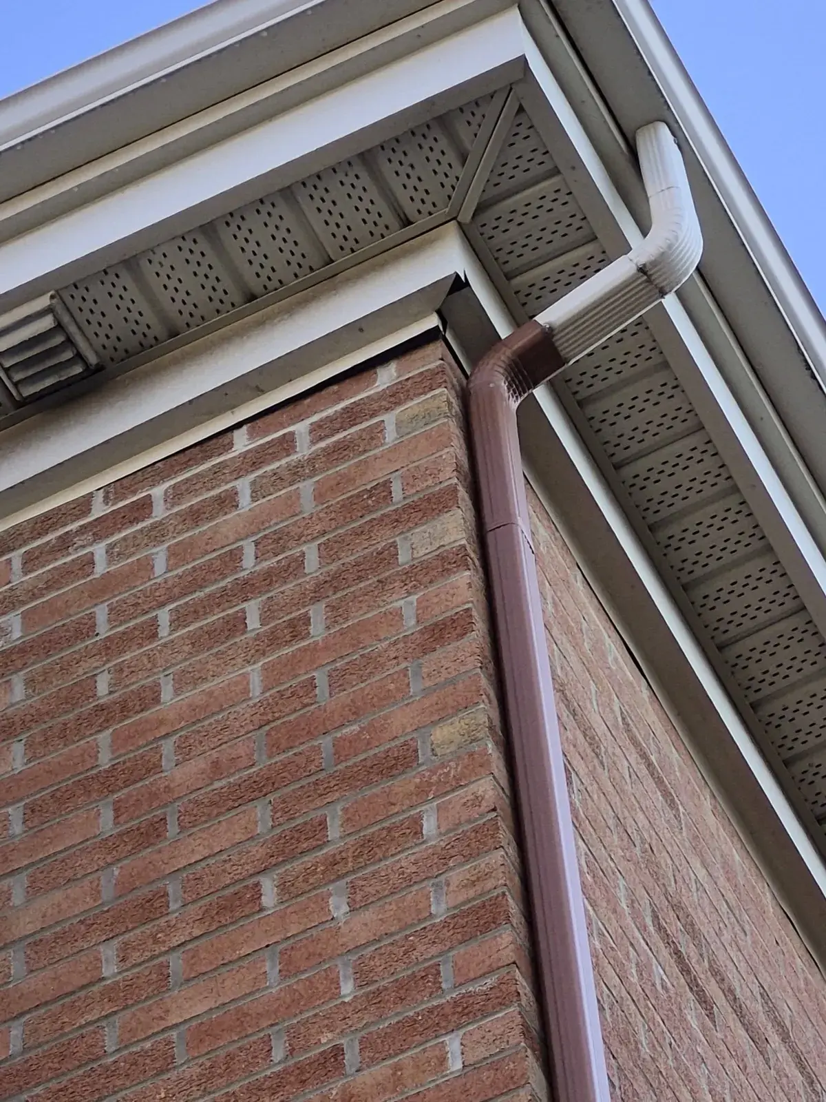 Descente pluviale raccordée à la gouttière et fixée au coin du mur de brique