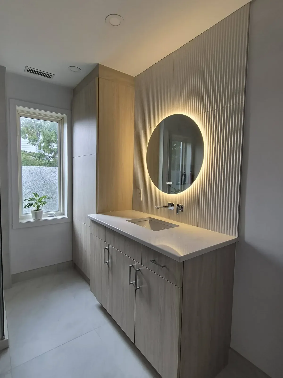 Vanité en bois clair et miroir rond éclairé sur un mur cannelé